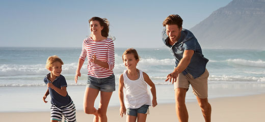 Parents running along beach with children on summer holidays